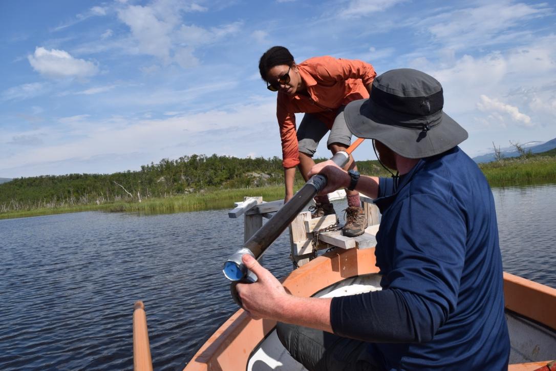 On a boat on a lake, two graduate students hold a research instrument